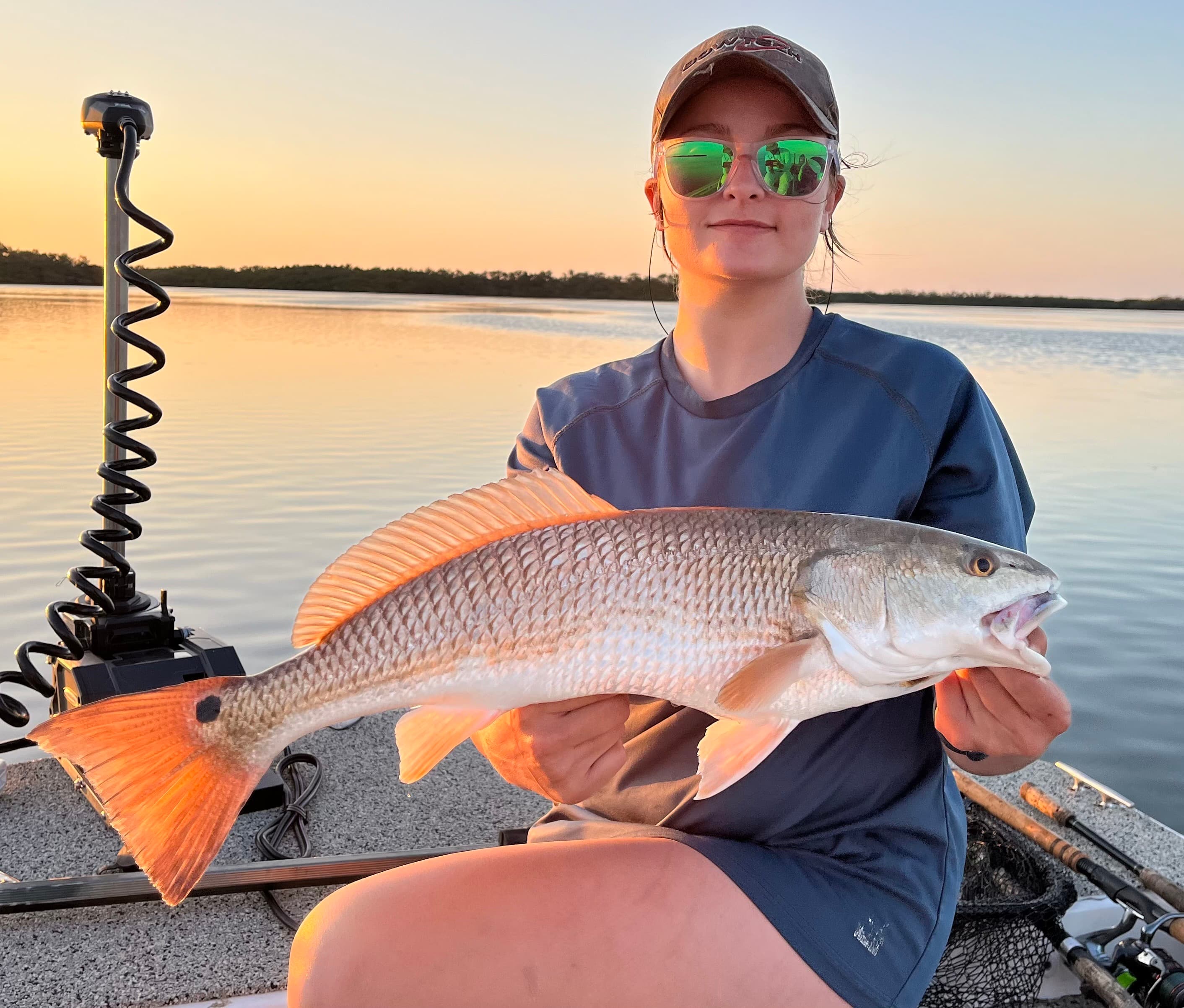 Angler holding a redfish aboard a Coyote fishing charter at sunset